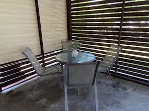 Relax in this serene outdoor seating area with a round table and four chairs, surrounded by a fence and a beautiful plant.