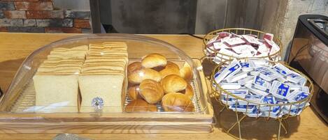 Un présentoir de petit-déjeuner avec du pain, des viennoiseries et des produits emballés, le tout disposé sur un comptoir en bois.
