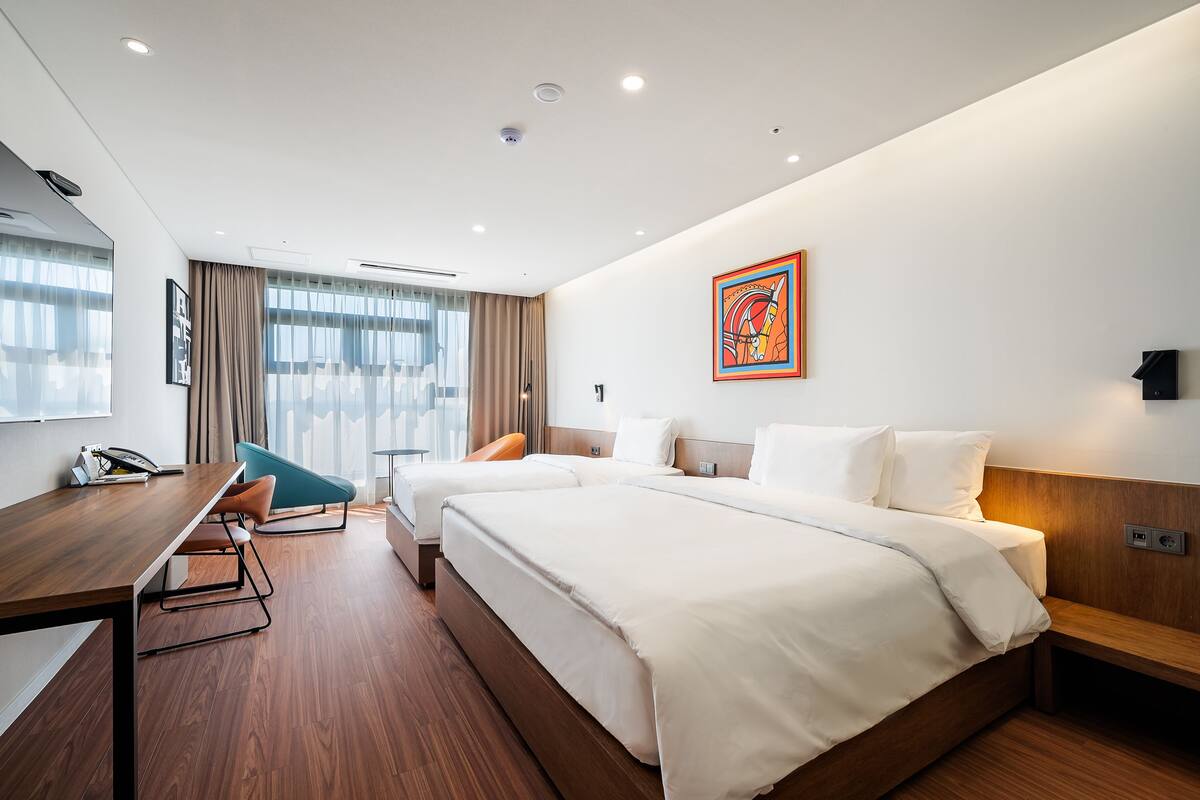 A modern hotel room with two beds, a desk, and a chair.