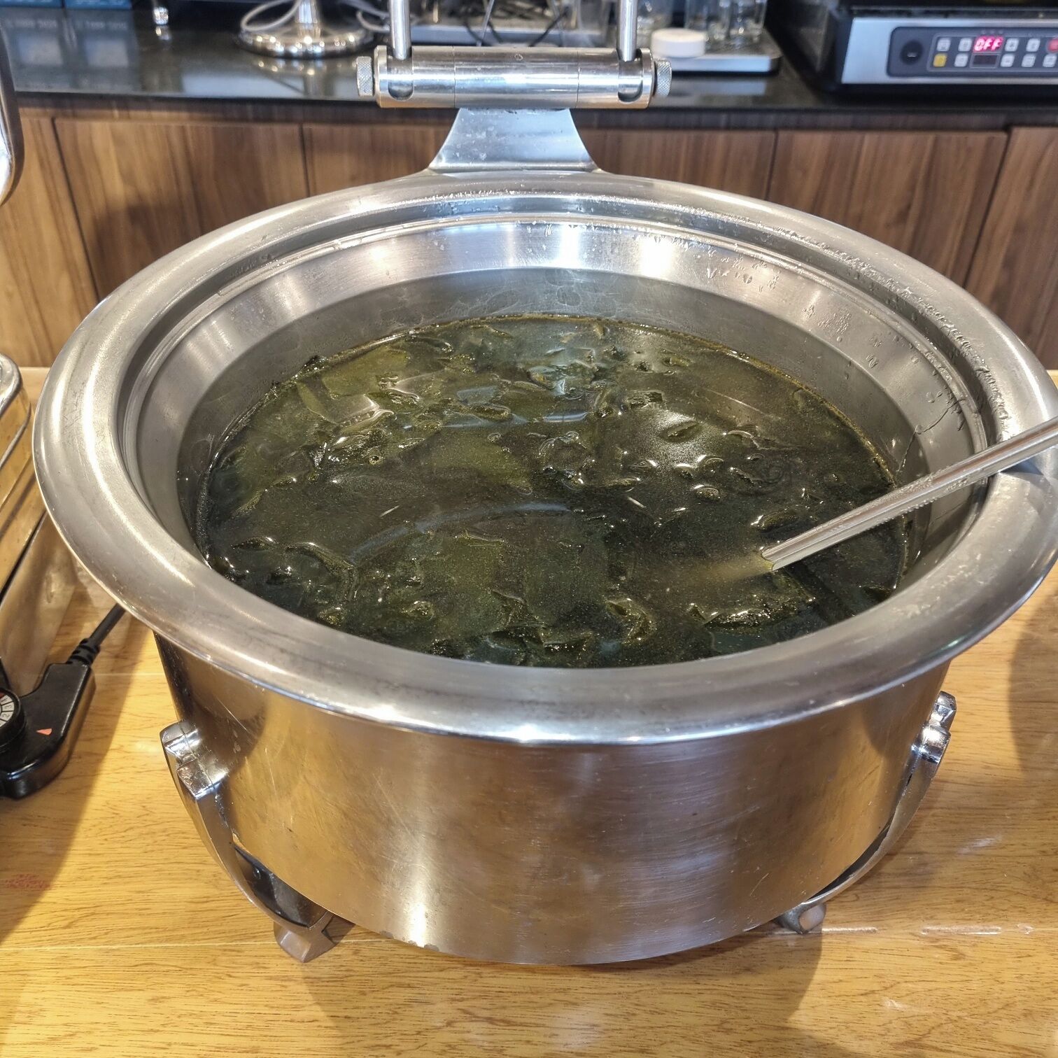 Una olla de cocción lenta de acero inoxidable con tapa sobre una encimera de madera.