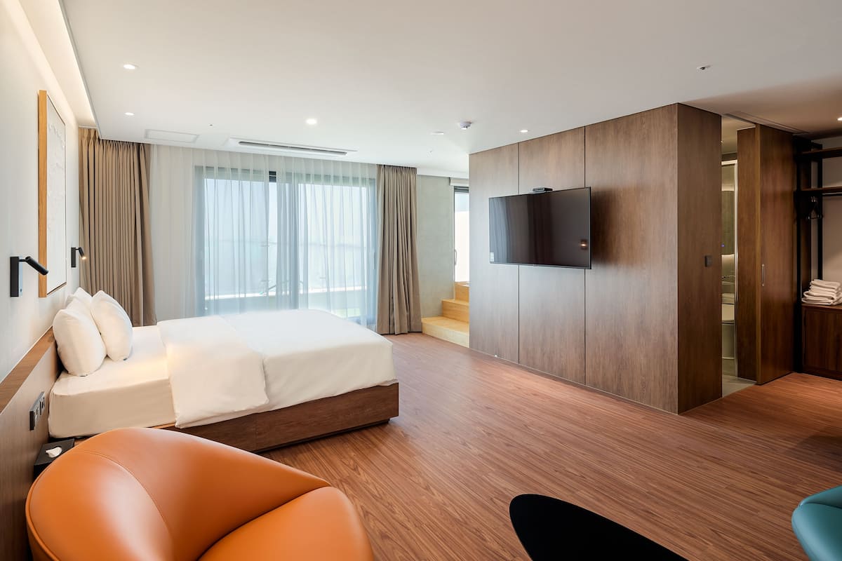 A modern hotel room with a large bed, a TV mounted on the wall, and a seating area with a chair and a sofa.