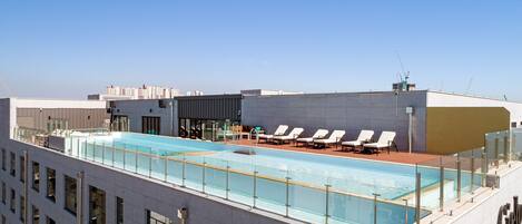 Una piscina en la azotea con sillones de descanso y una vista despejada del horizonte de la ciudad.