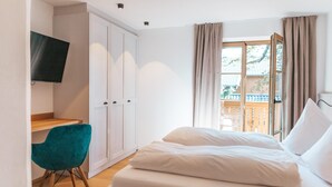 Un dormitorio con cama, escritorio, silla, televisor y ventana con cortinas.