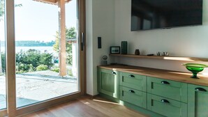 Een moderne keuken met een schuifdeur naar een terras, een flatscreen televisie aan de muur en een houten aanrechtblad met een groene kom.