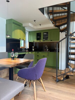 A modern kitchen with green cabinets, a wooden dining table, and a purple chair.