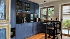 A modern kitchen with dark blue cabinets, a black countertop, and a bar area with stools. - Garden Suite with cozy eat-in kitchen and lake view (Frauenchiemsee)