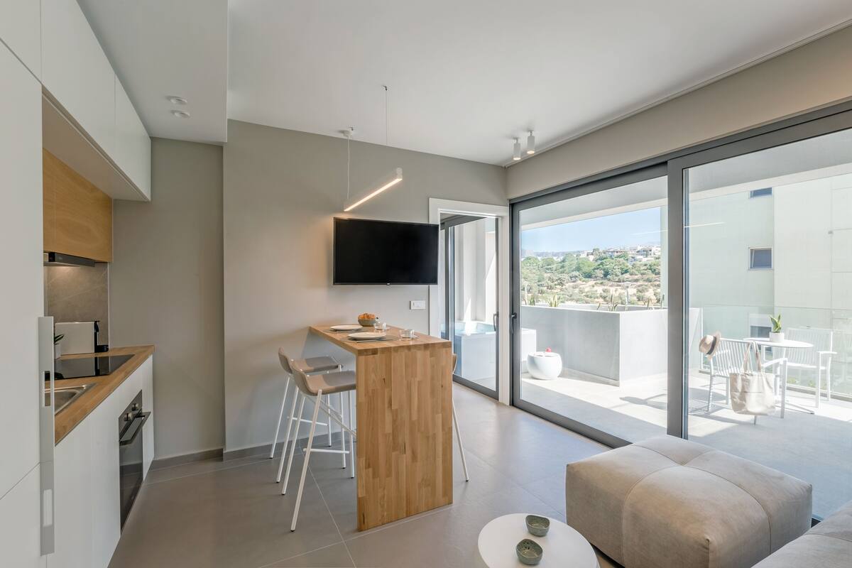 Una cocina moderna con una isla de madera, un televisor de pantalla plana y una zona de comedor con taburetes de bar.
