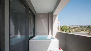 Ein moderner Balkon mit integriertem Whirlpool, einer Glastür und Blick auf die Landschaft.