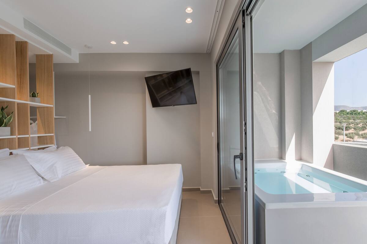 Un dormitorio moderno con cama, televisor y jacuzzi con paredes de vidrio.
