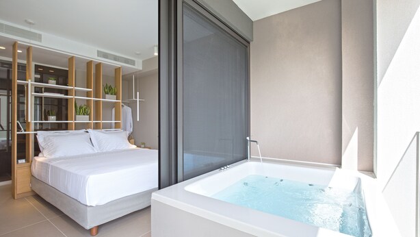 Ein modernes Schlafzimmer mit großem Bett, einem separaten Badezimmer mit Badewanne und einer Glastür, die auf einen Balkon führt.