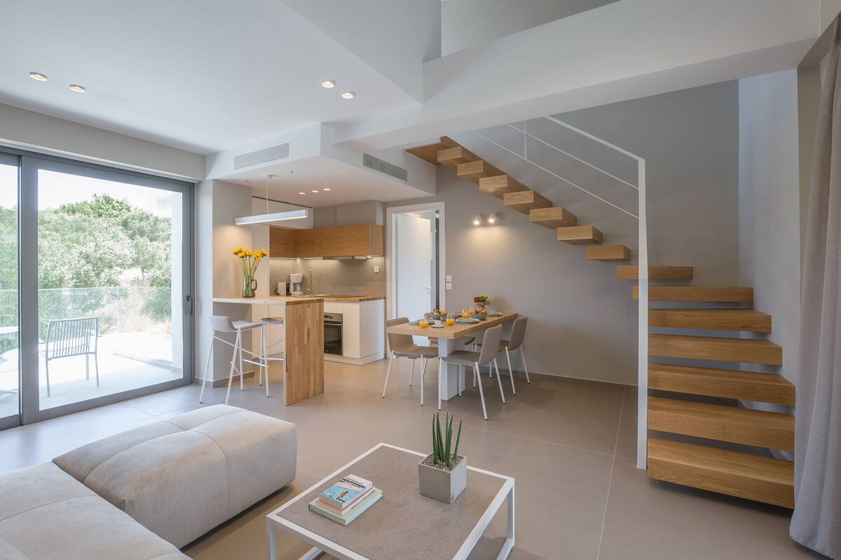 Un interior moderno con una escalera, una zona de comedor y un espacio de sala con un sofá y una mesa de centro.