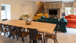 A modern living room with a wooden dining table, black chairs, a green sofa with orange cushions, and a stone fireplace.