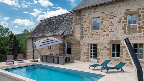 A stone house with a swimming pool, outdoor seating, and a clear sky.