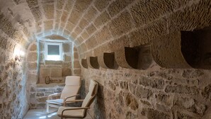 A stone-walled room with a small window, two white chairs, and a stone bench.