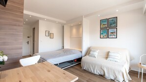 A modern, compact room with a wooden dining table, a bed with a pull-out desk, a sofa, and a small white chair. - Les Pradels by Interhome (Cavalaire)
