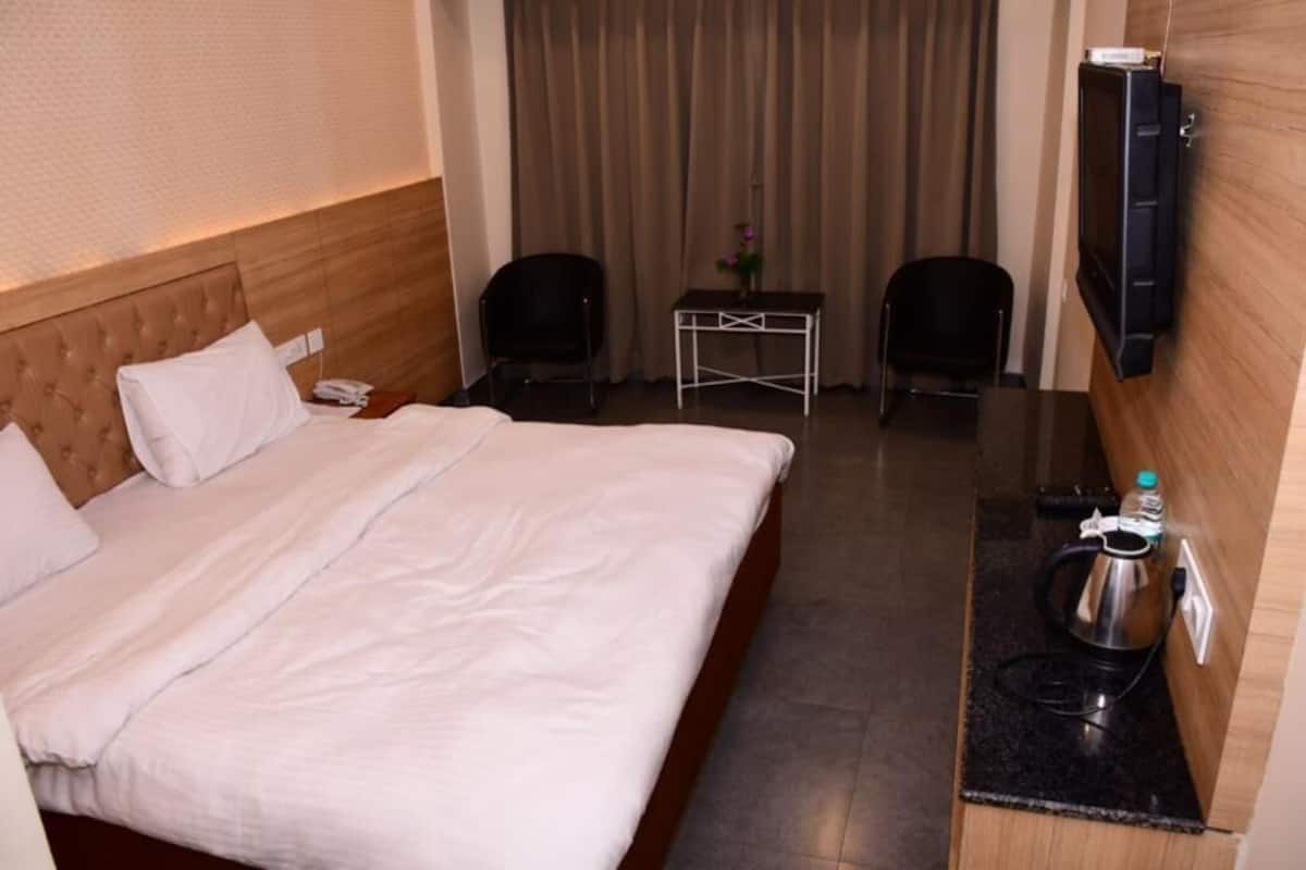 A hotel room with a bed, a small table with chairs, a television, and a kettle on the side table.