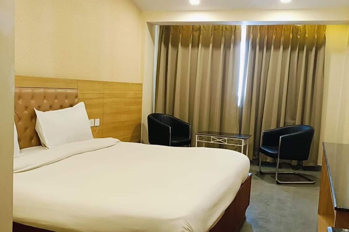 A hotel room with a large bed, two chairs, a small table, and a curtain.