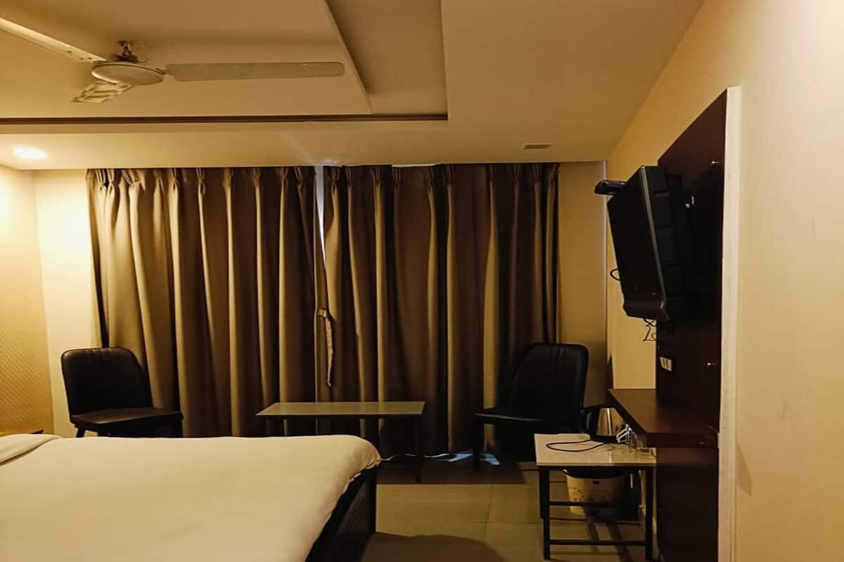 A hotel room with a bed, a desk, two chairs, a television, and curtains.