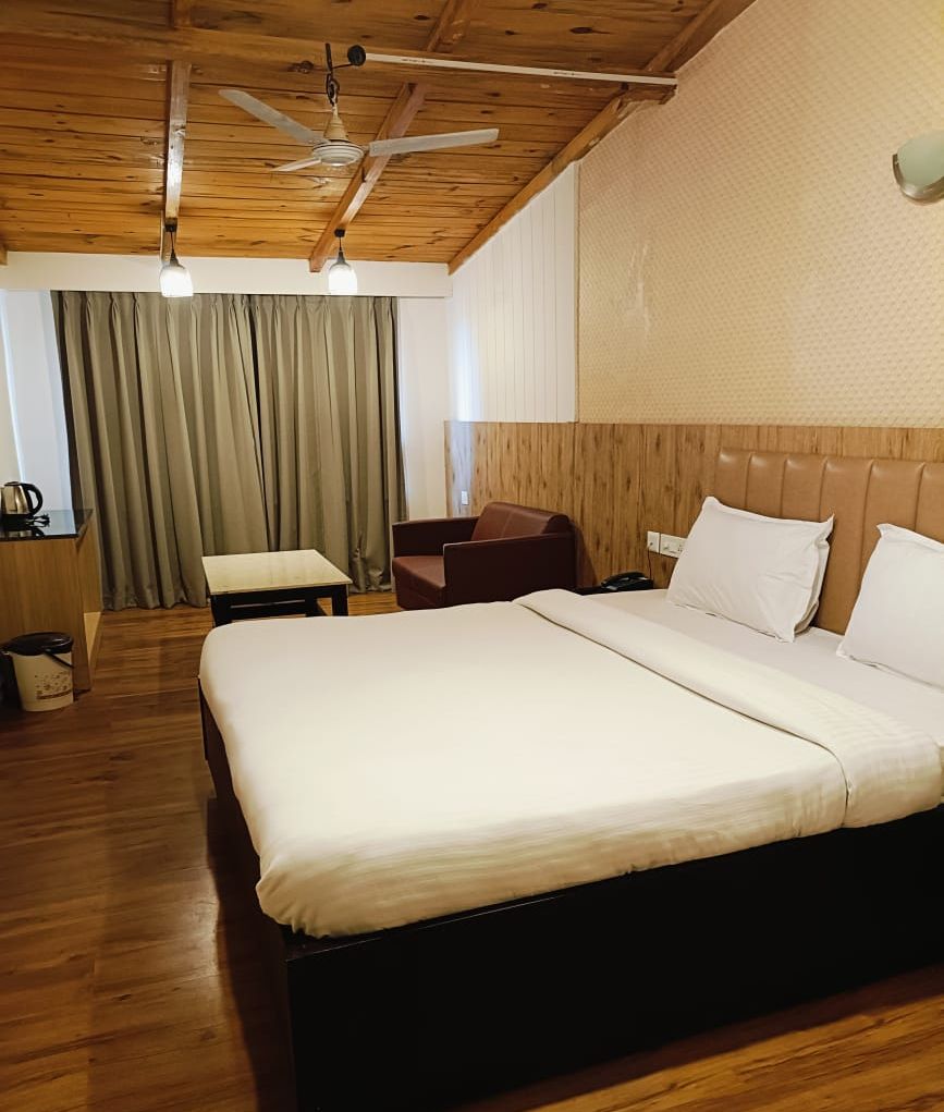 Quarto de hotel com cama grande, teto de madeira, escrivaninha e uma cadeira.