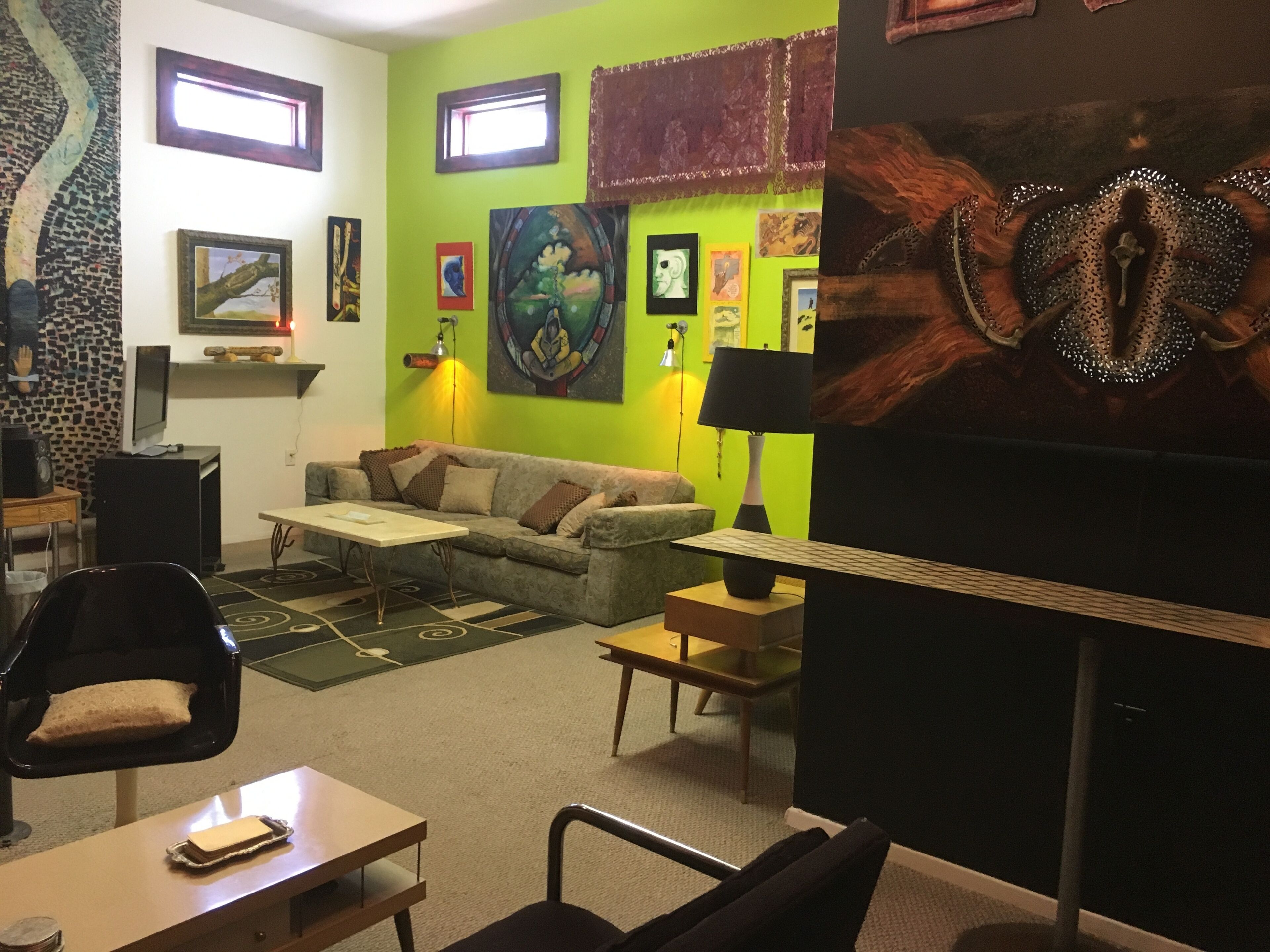 Ein Wohnzimmer mit grüner Wand, einer Couch, einem Couchtisch, einem Fernseher und verschiedenen Kunstwerken.