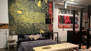 A bedroom with a bed, a table, and chairs. There are paintings on the walls.