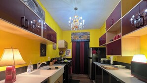 A compact kitchen with yellow walls, a chandelier, and a striped rug.