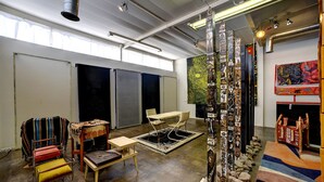 An art gallery with a central sculpture, a table with chairs, and a colorful rug.