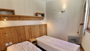 A room with two single beds, wooden headboard, a small wooden nightstand, a wall-mounted light fixture, and a window with a curtain. - Comfortable 2 Rooms + Cabin, Pets Allowed, Ski-in/Ski-out (La Tania)