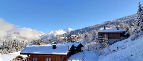 A wooden cabin with a balcony, surrounded by snow-covered trees and mountains in the background.