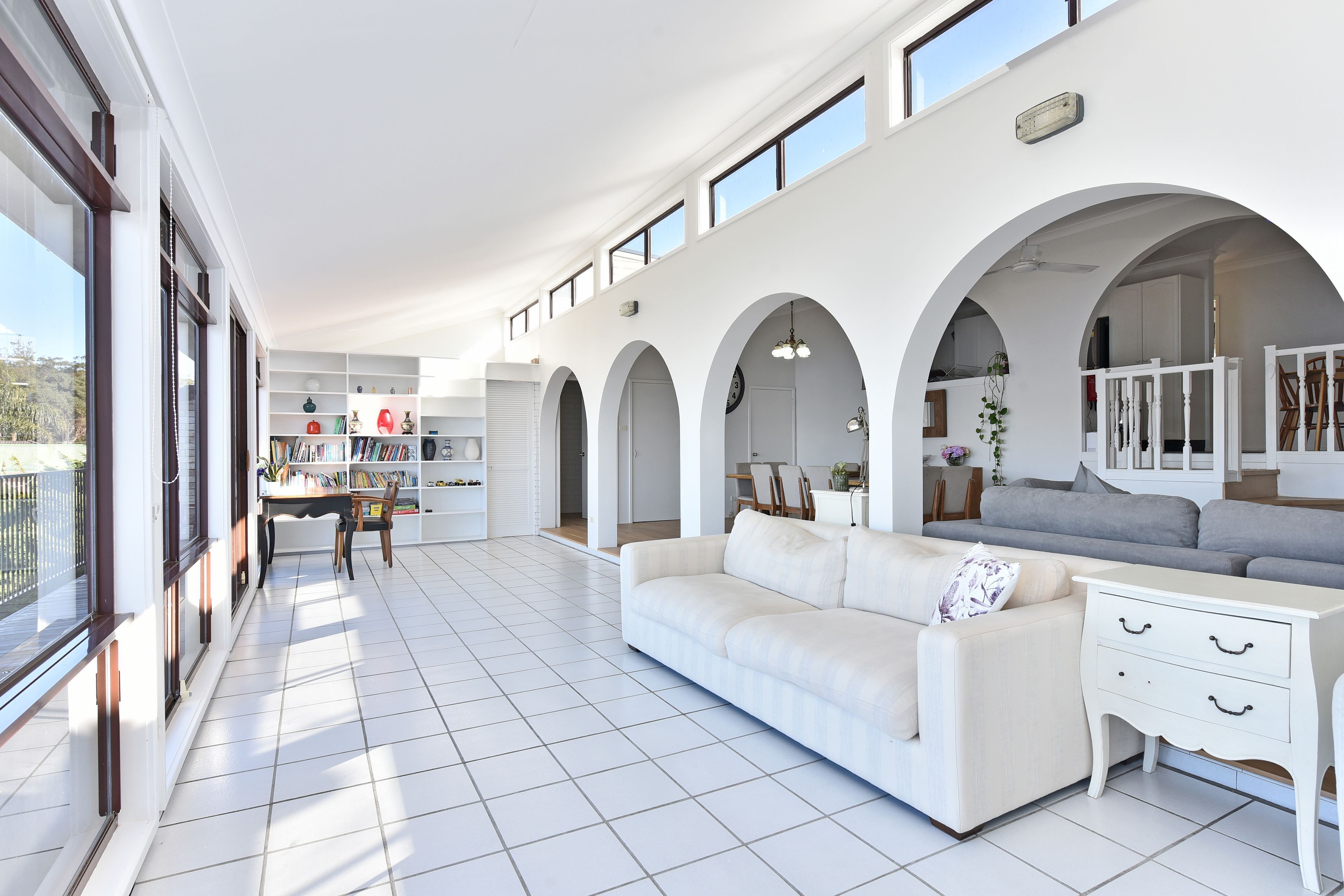 A spacious living area with a white sofa, a dining table, and a kitchen in the background.