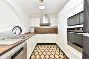 A modern kitchen with white cabinets, a built-in oven, a microwave, and a patterned floor. - Sunshine Shores Absolute Waterfront (Sunshine)