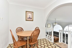 A dining area with a round table and wooden chairs, a framed picture on the wall, and a staircase leading to a balcony with a white railing. - Sunshine Shores Absolute Waterfront (Sunshine)