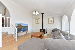 A modern living room with a fireplace, a television, and a staircase. - Sunshine Shores Absolute Waterfront (Sunshine)