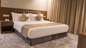Una camera d'albergo con un letto, un comodino e un'ampia finestra con tende.