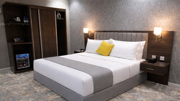 Ein Hotelzimmer mit Bett, Schrank, Nachttisch und einer Wandlampe.