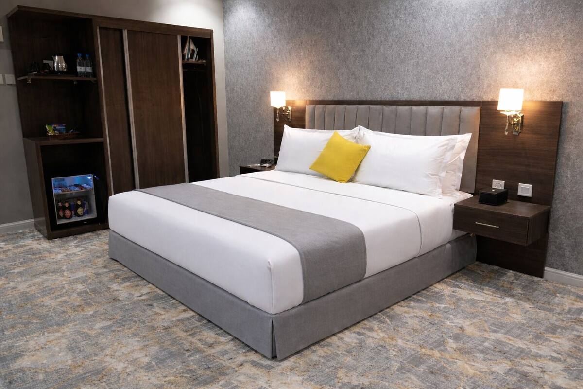 A hotel room with a bed, a wardrobe, a nightstand, and a wall-mounted lamp.