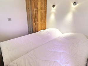 A bedroom with a wooden door, a bed with white bedding, and two wall-mounted light fixtures.
