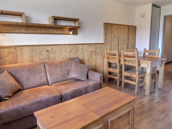 A cozy room with a wooden sofa, a wooden dining table with chairs, and a wooden bench.