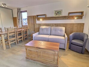 A room with a wooden sofa, a grey armchair, a wooden coffee table, a dining table with chairs, and a wooden wall panel. - Comfortable 2 Rooms + Cabin, Ski to Door, 5-6 People (La Tania)