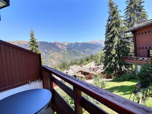 A balcony with a view of mountains, a wooden deck, and a small table.