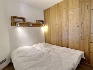 A bedroom with a wooden panel wall, a bed with white bedding, and two wall-mounted light fixtures.