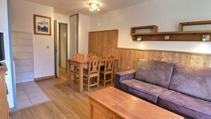 Een woonkamer met een houten tafel, een paarse bank en een houten kast.