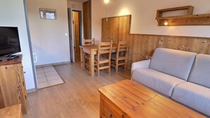 Un saló tranquil amb un sofà de fusta, una taula baixa de fusta i una zona de menjador amb una taula i caires de fusta.