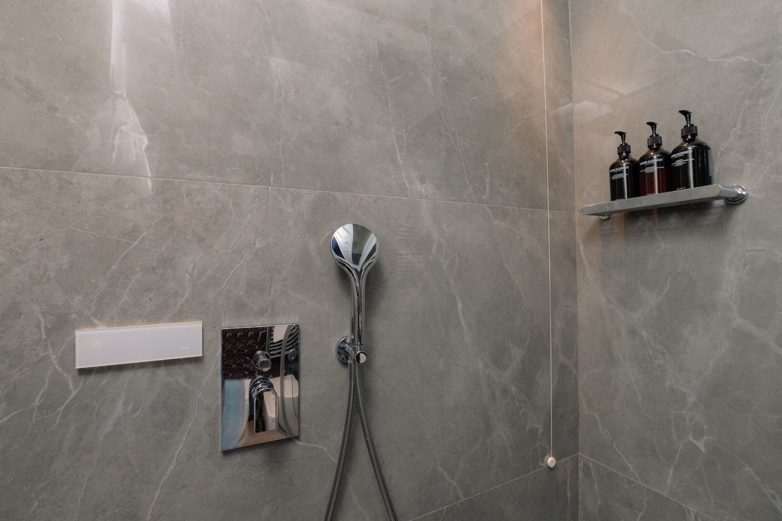 A bathroom with a shower, a mirror, and a shelf with toiletries.
