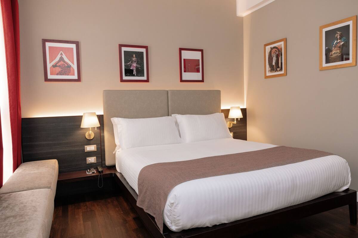 A hotel room with a large bed, two bedside tables with lamps, a small sofa, and framed pictures on the walls.