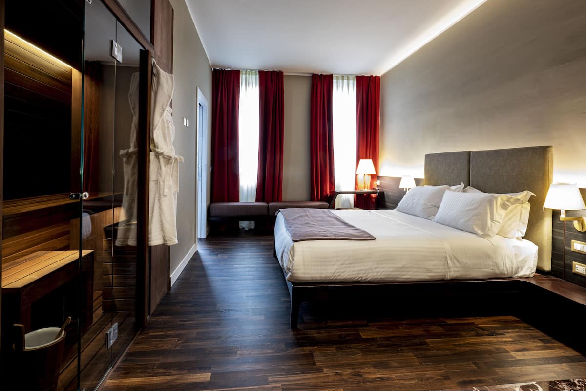 A hotel room with a bed, bedside tables, a robe, a seating area, and a view of the outside through large windows.