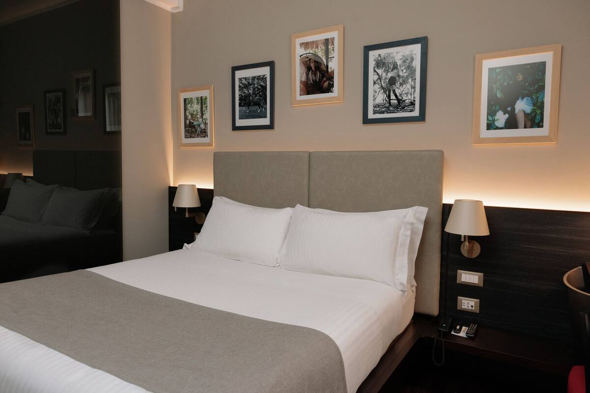 A hotel room with a large bed, bedside tables, and framed pictures on the wall.