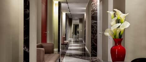 En modern hotellobby med ett marmorgolv, en receptionsdisk, en sittgrupp och en vas med vita blommor.