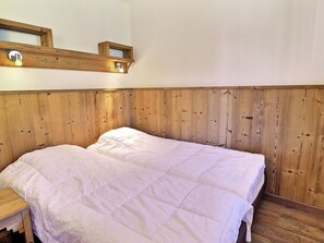 A room with a wooden headboard, a bed with white bedding, a wooden nightstand, and a wall-mounted shelf with a light fixture.