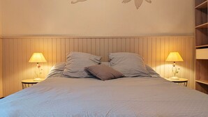 A bedroom with a bed, two bedside tables with lamps, a wooden headboard, and wall art of birds.